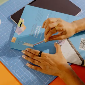 Händer som öppnar förpackningen till ett Paperlike-skärmskydd över en iPad på en skärmatta