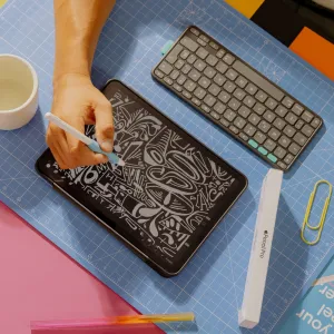 Paperlike skjermbeskytter til iPad vist i et kreativt arbeidsområde, med en pekepenn som tegner på et nettbrett ved siden av et tastatur.