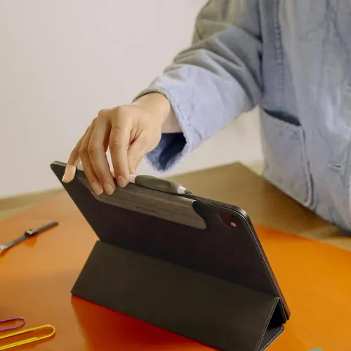 Ergonomiskt penngrepp i mörkgrått på Apple Pencil som magnetiskt fästs längs surfplattans kant på ett svart vikbart fodral.