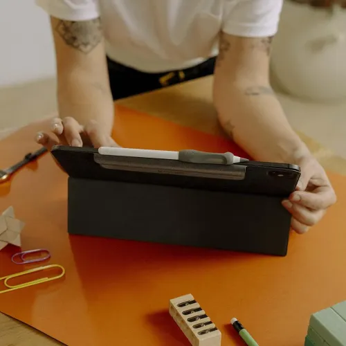 Ergonomiskt grått penngrepp för Apple Pencil sitter på en vit penna som magnetiskt vilar ovanpå ett iPad-fodral i stödläge.