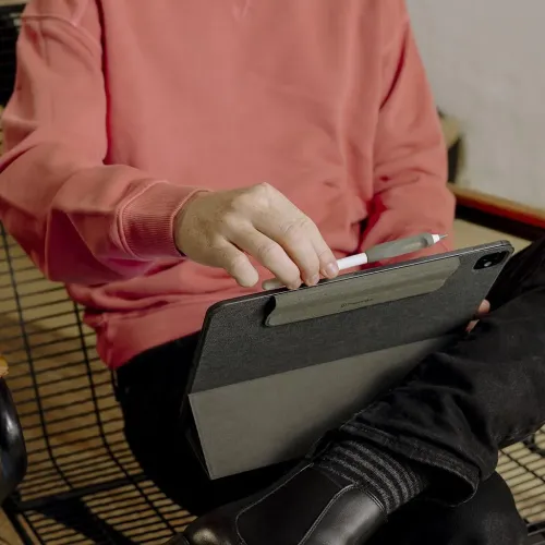 Paperlike Pencil Grips V2 i kol, grått grepp på vit stylus, hålls mot surfplattans kant i fodral; greppets form och placering.