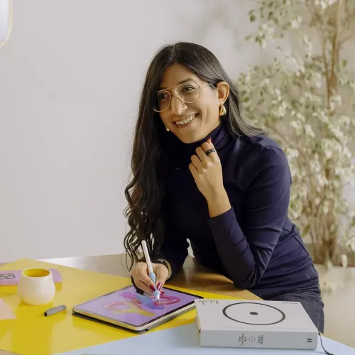 Blått penngrepp för Apple Pencil sitter på stylus som används på surfplatta; produktlådan syns bredvid på ett bord i bild.